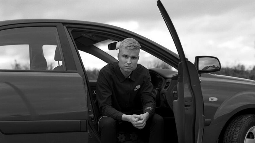 Black and white photo of For Those I Love- aka David Balfe - half-sitting in the drivers seat of an open car