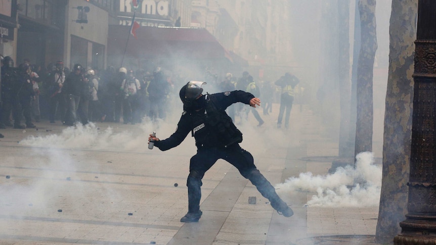 A riot police officer throws a tear gas canister.