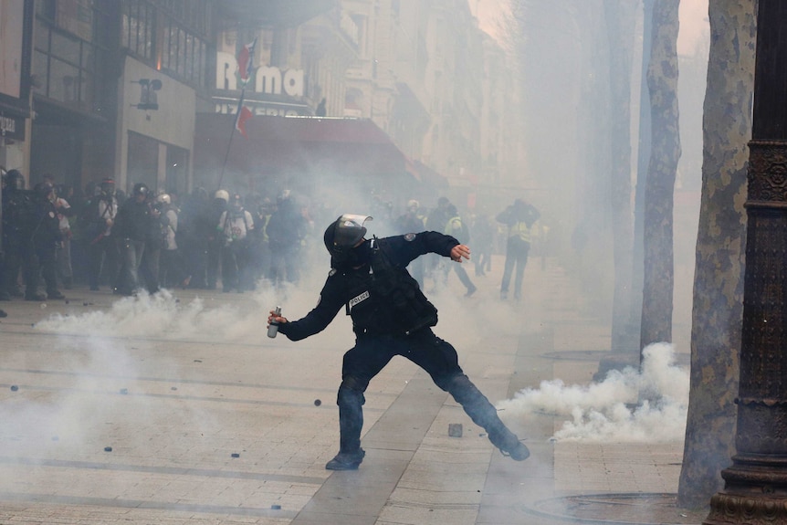 A riot police officer throws a tear gas canister.