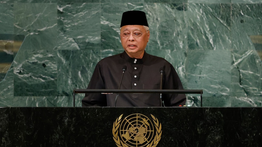 Malaysia's PM standing in front of microphone for a speech. 
