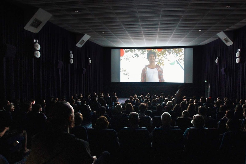 A photo of a film screening in a packed out, darkened cinema.