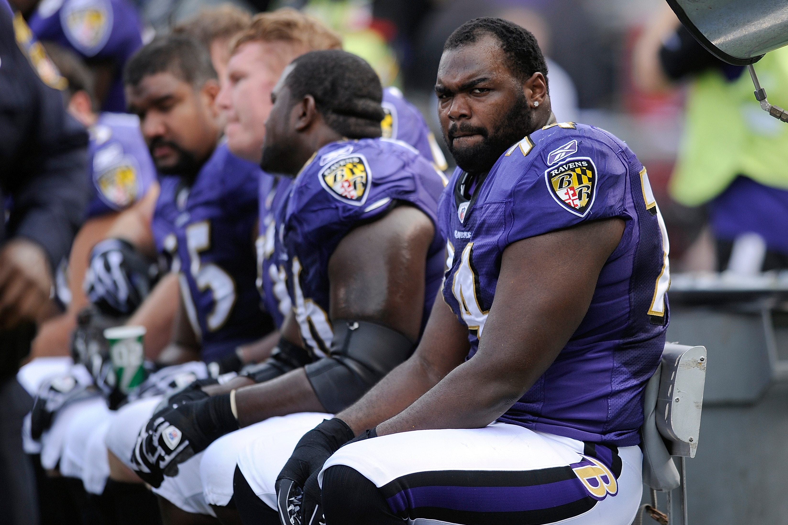 A man wearing a purple american football outfit grimicing while sitting on a bench next to other players