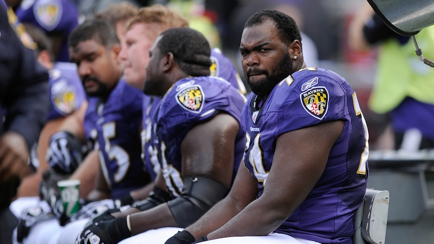 A man wearing a purple american football outfit grimicing while sitting on a bench next to other players