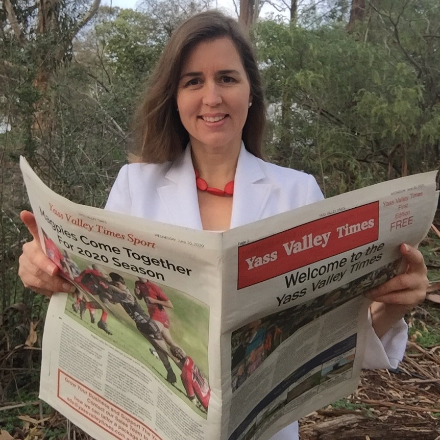 A woman holds a Yass Valley Times newspaper open in front of her.