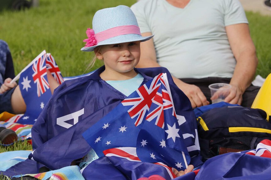 A girl draped in Australian flags sitting on grass nearby other people