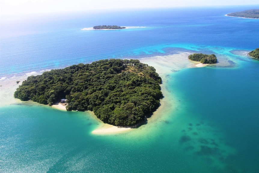 An aerial image of a picturesque vanautu island with lush green bushland surrounded by white beach and crystal clear waters