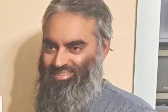 Junaid Ismail smile. He has a long brown and grey beard, with short and similarly coloured hair.