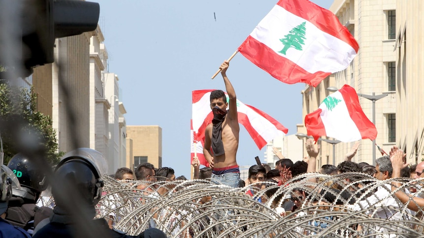 Lebanese protesters wave the national flag in front of a barbed wire fence during a demonstration