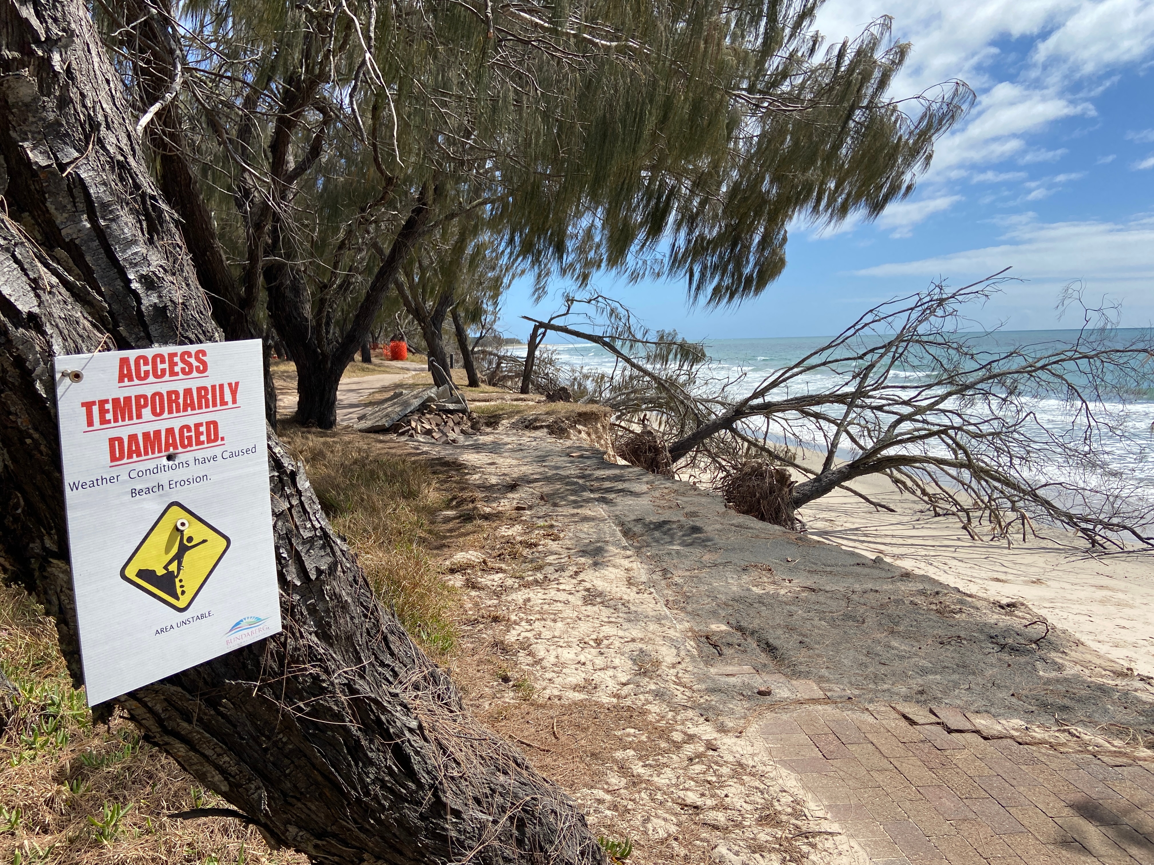 An Access Temporarily Damaged Sign next to the broken brick footpath from sand being eroded beside it.