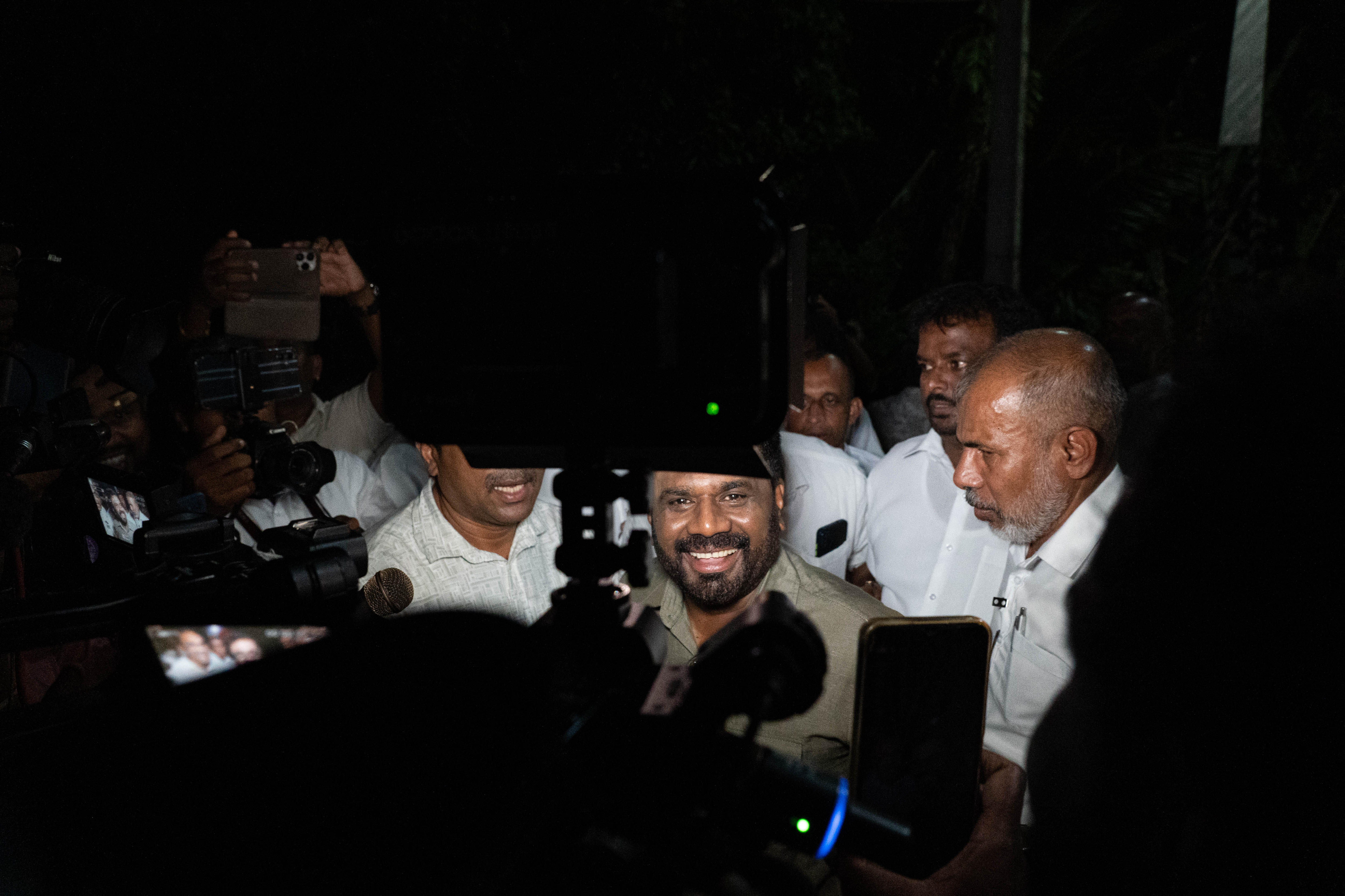 A man smile widely in front of a group of people and TV cameras