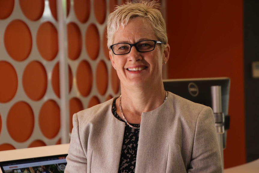 A head and shoulder shot of a smiling Donna Dalby with an orange and silver office background.