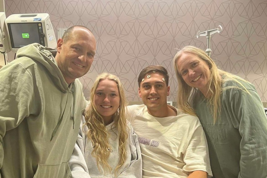 A family smiling at the camera from a hospital room. Two men and two women.