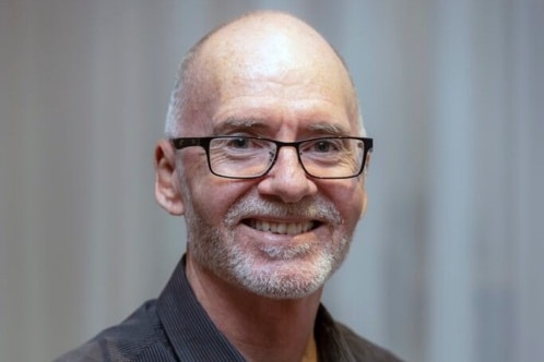 Headshot of Peter Gartlan. He wears a dark button up shirt and glasses.