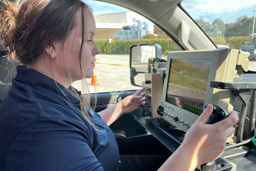 Woman inside a pickup truck looking at a screen with her hand on a joystick.