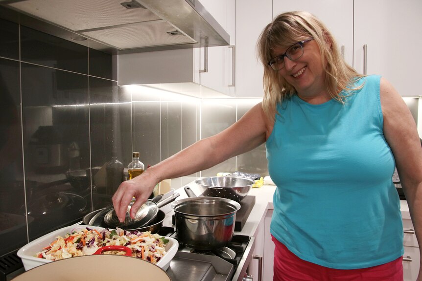 Woman stands in the kitchen in front of food cooking on the stove