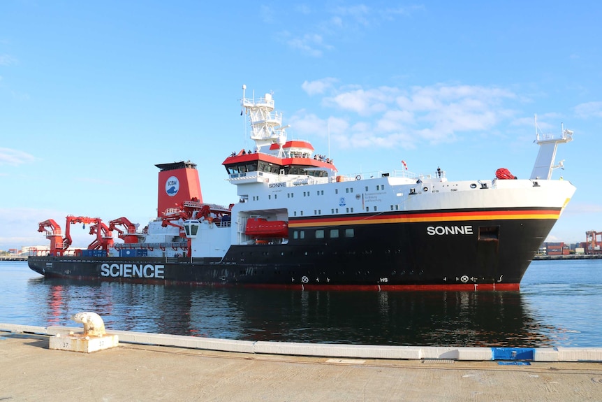 A large black, red, white and yellow German deep sea research vessel, the RV Sonne, sails into Fremantle Port under a blue sky