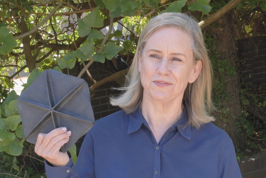 Water Minister Simone McGurk holding a black plastic disk in the shape of a hexagon 