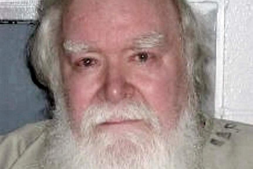 A mugshot of an older man with a big bushy beard 