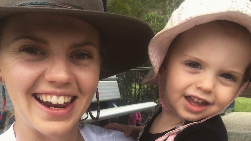 A woman wearing a hat with her toddler in a park.