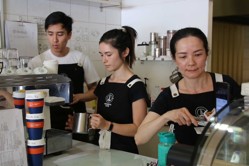 A man and two women work making coffee at a cafe.