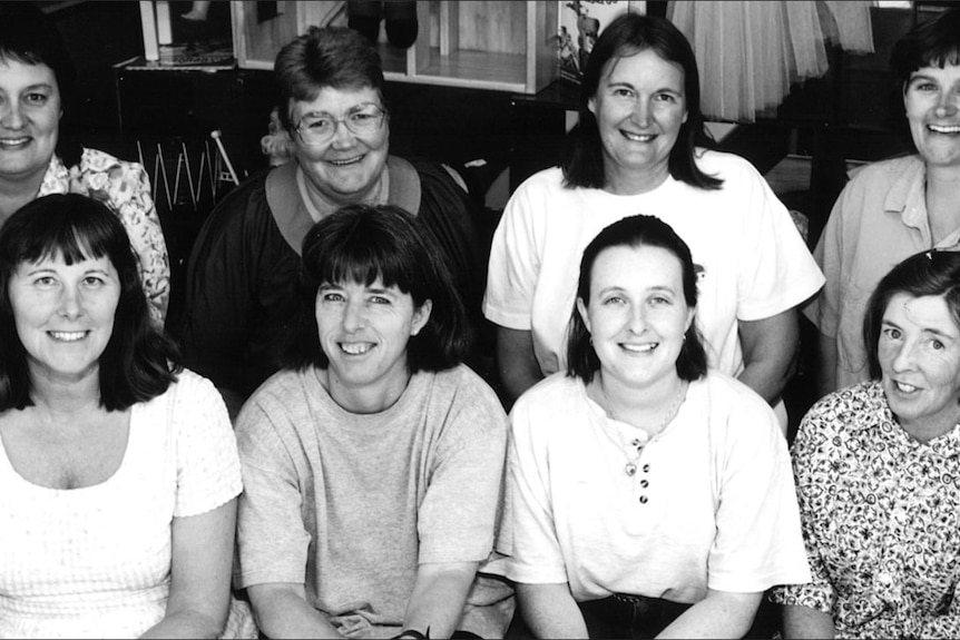 Eight women sit smiling in a black and white photo.