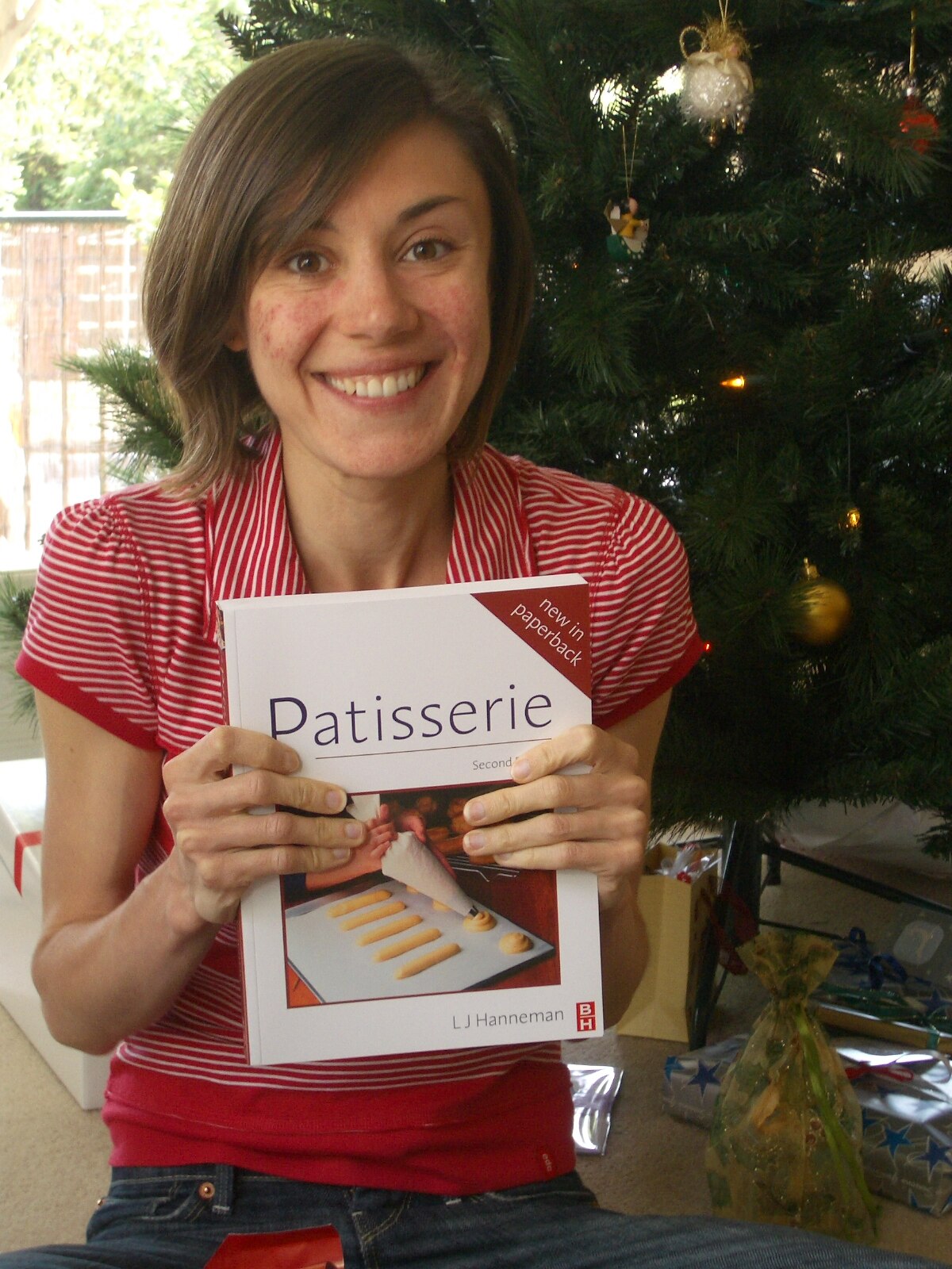 A woman wearing a pink tv shirt holding a pastries book looks visibly thin