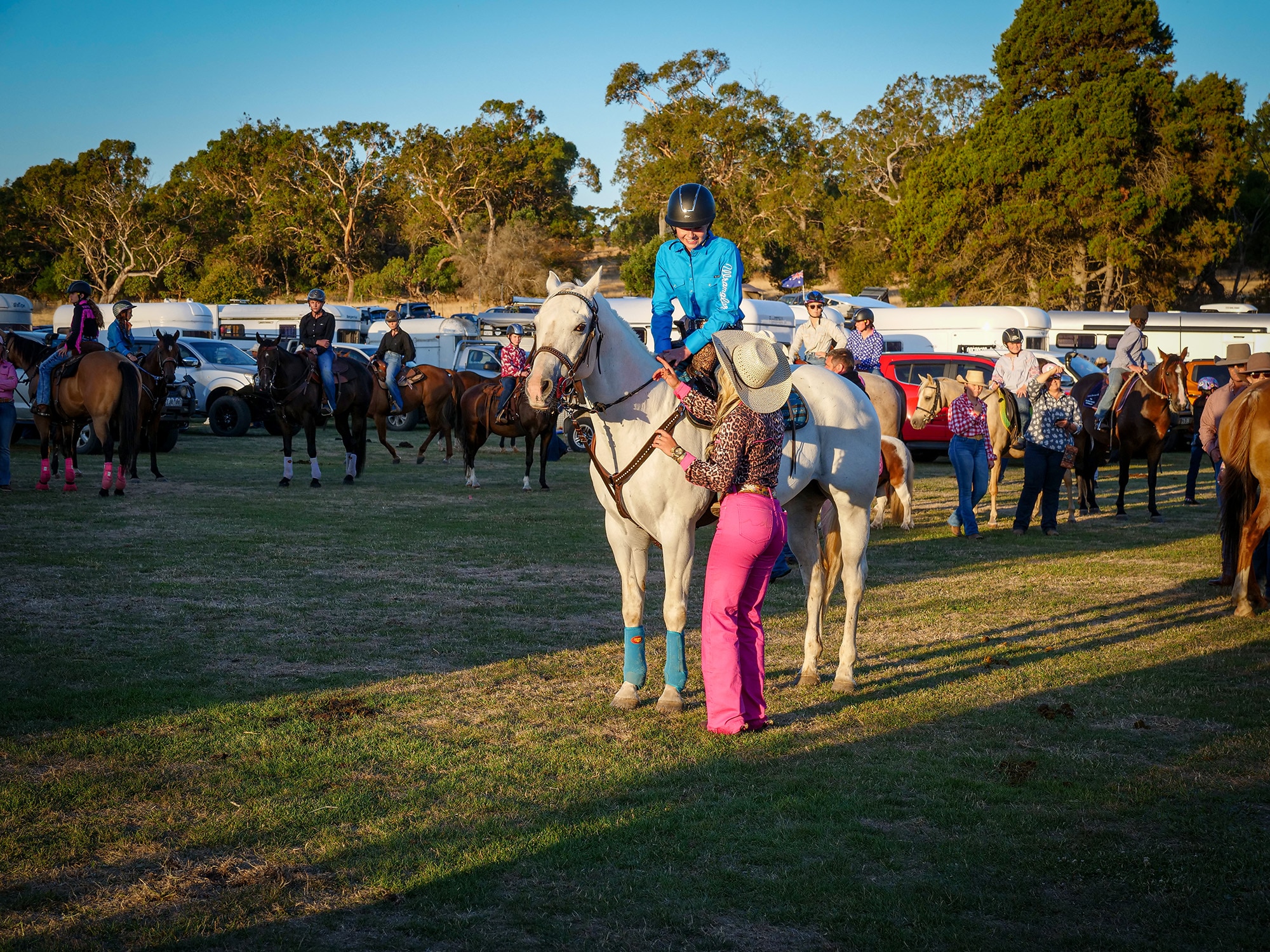 A woman wearing bright pink jeans speaks to a woman riding a horse.