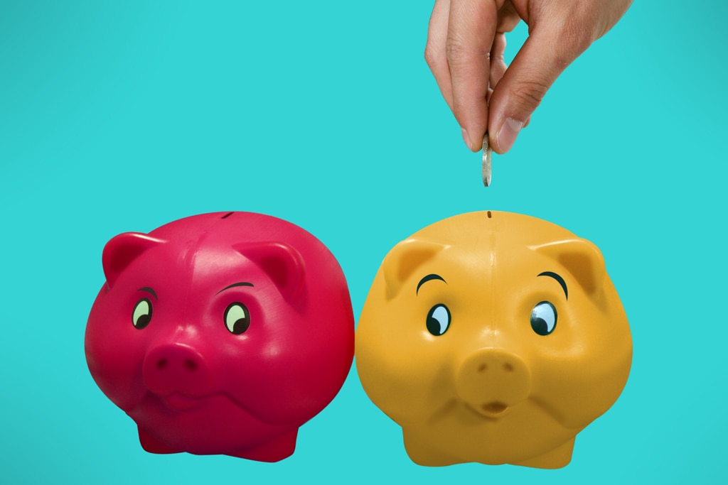 Two piggy banks with a hand feeding a coin into one.