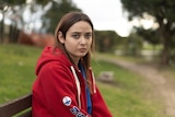 Woman wearing a red hoodie, sitting on a park bench.