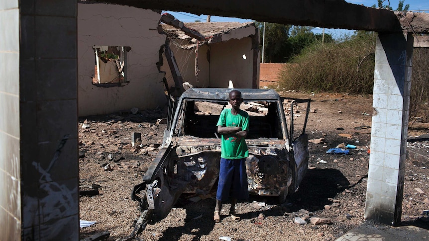 Boy stands beside charred vehicle in Mali