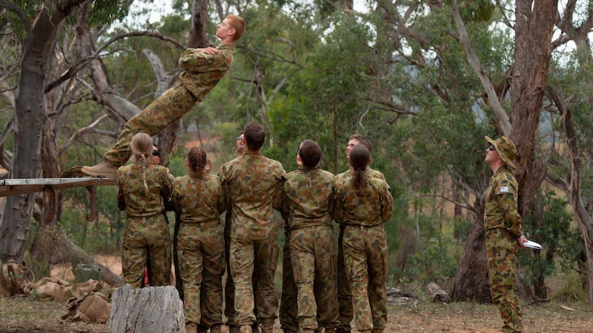 Boy leans backward for trust exercise where eight soldiers in training are preparing to catch him