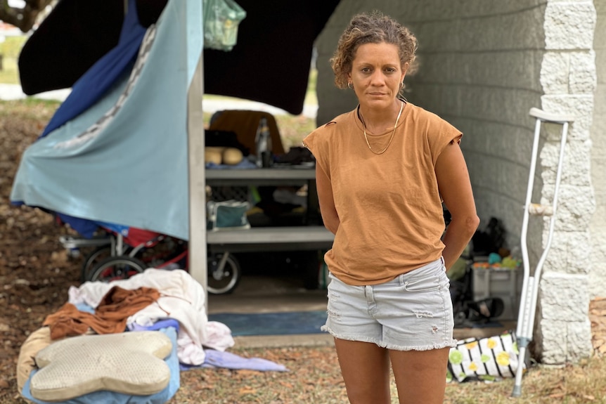 Homeless woman standing in front of shelter shed containing her belongings.
