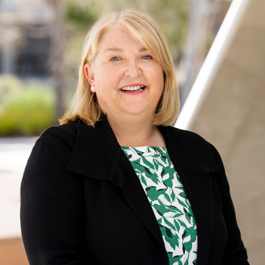  A middle aged woman with blonde hair, wearing a black blazer smiles at the camera