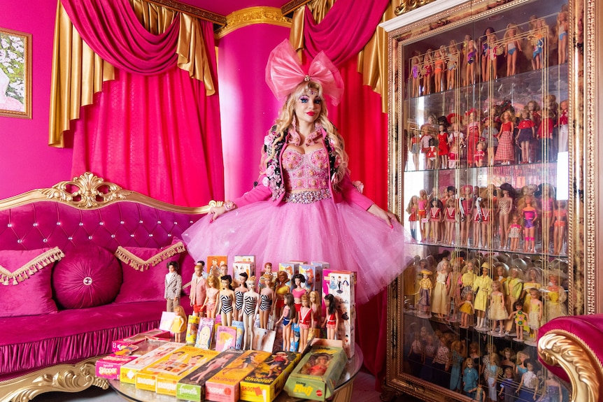 Woman poses in front of hundreds of barbie dolls