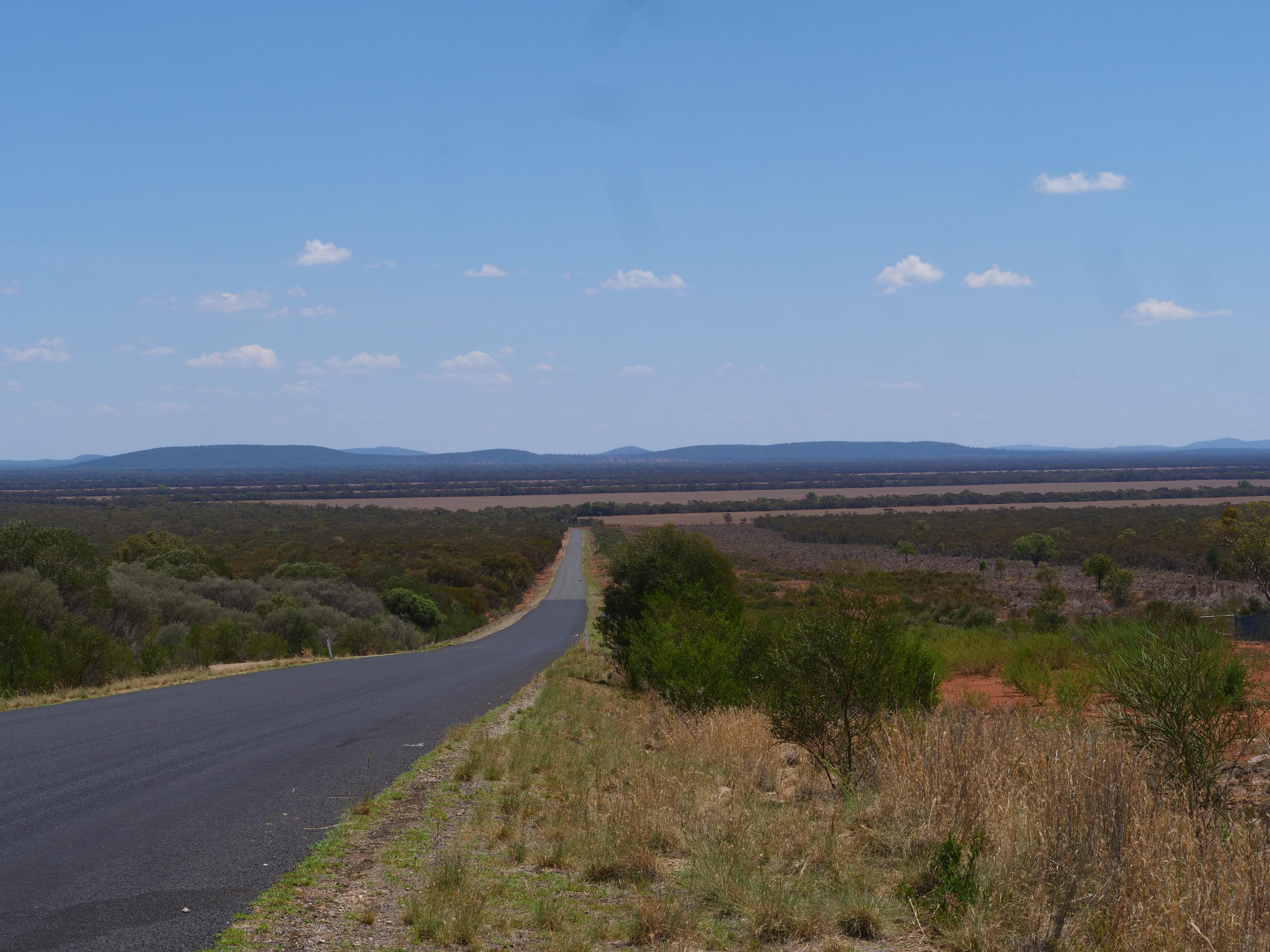 Ao longe encontra-se um local isolado, rodeado de mato rasteiro e com grandes colinas ao fundo.