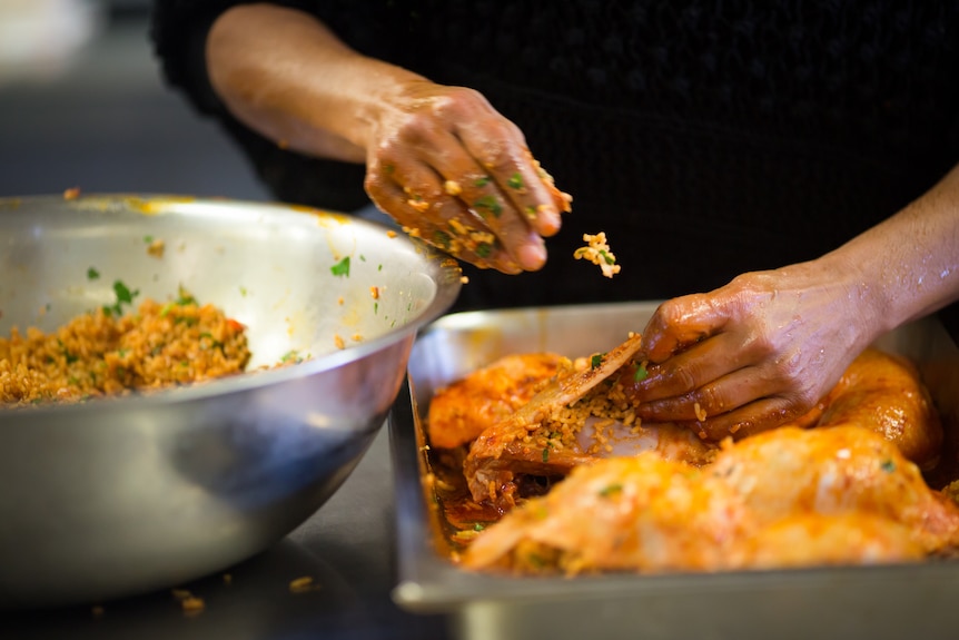 A piece of rice in mid air as hands stuff chicken richly coloured with paprika.