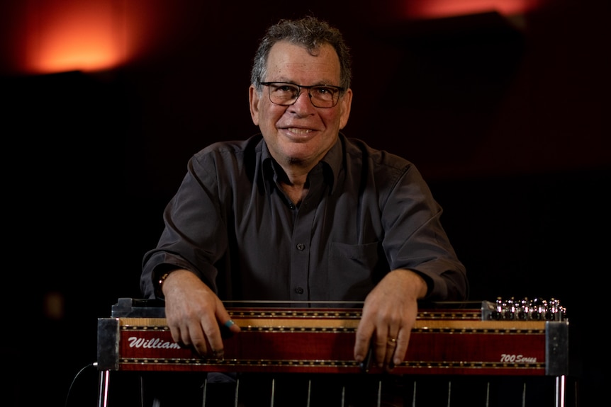 Lucky Oceans sits smiling and learning forward over his pedal steel guitar. 