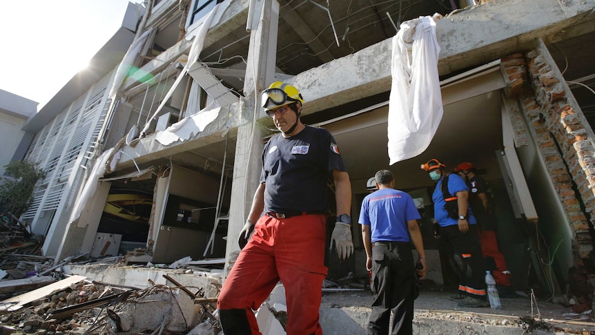 A rescuer wearing a protective helmet walking out of a hotel destroyed in the Indonesian earthquake and tsunami.