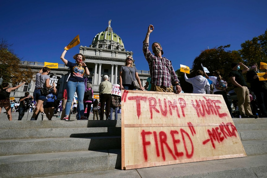 Man stands with placard reading 'Trump you're fired'.