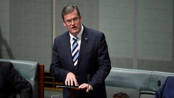 A man in a suit speaks at a podium in the House of Representatives.