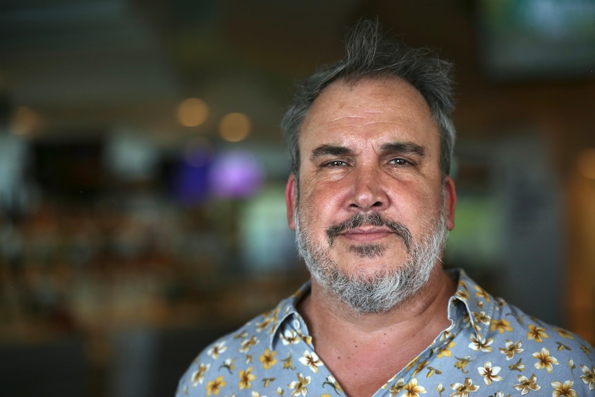 Un hombre con barba canosa y camisa de cuello azul posa para una foto