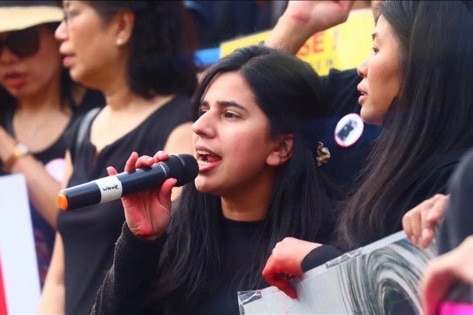 A woman speaks into a microphone from a crowd.