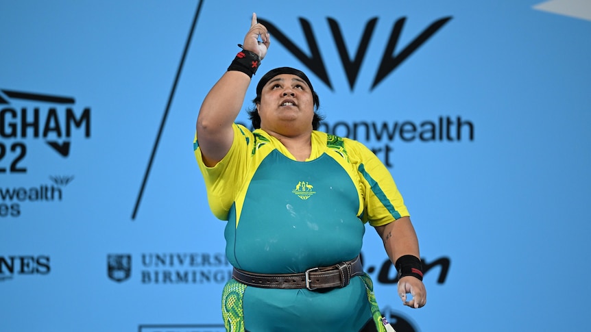 An Australian weightlifter stands on stage and points her finger to the sky after clinching a Commonwealth Games medal.