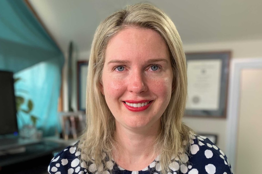 A portrait of a smiling woman sitting in an office wearing bright red lipstick.