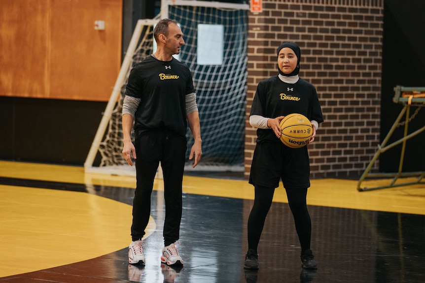 Sabera stands on court next to a coach, holding a basketball.