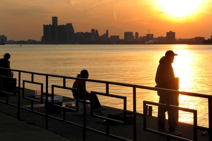 People fish as the sun sets over the city of Detroit.