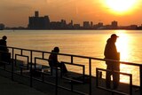People fish as the sun sets over the city of Detroit.