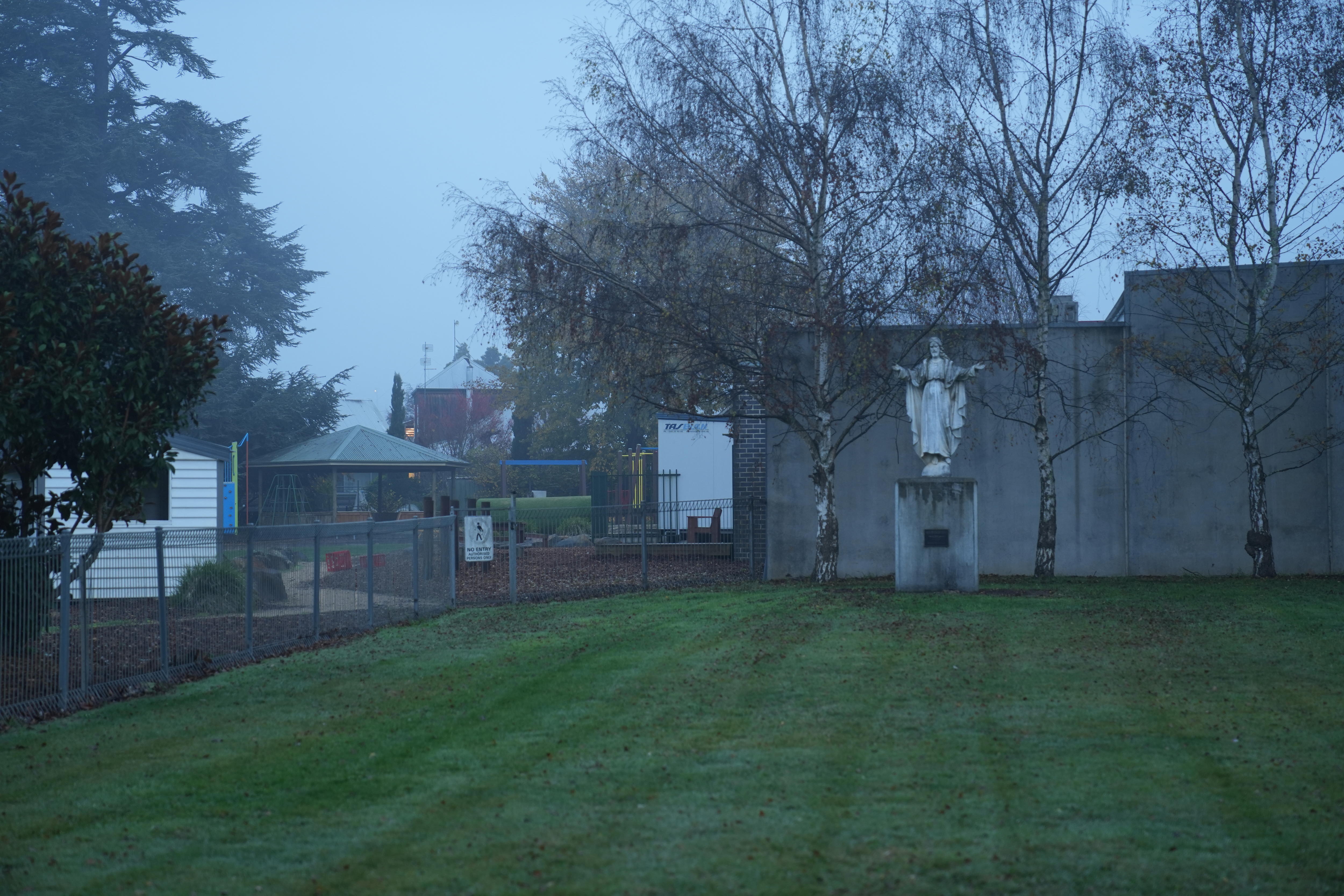 A memorial sits in a churchyard, with a school behind