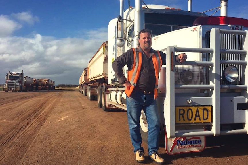Man in high-vis vest stands beside huge truck on dirt road