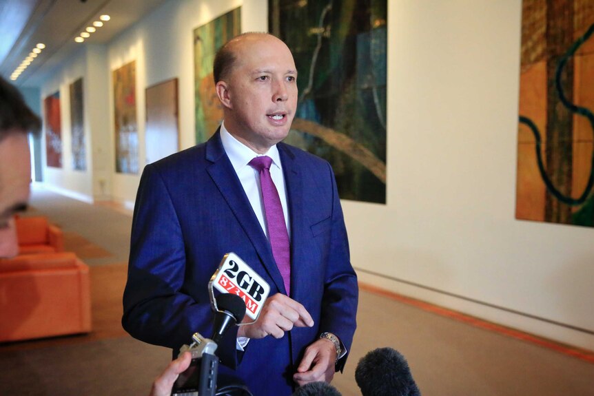 Peter Dutton stands and speaks to media in a hallway.
